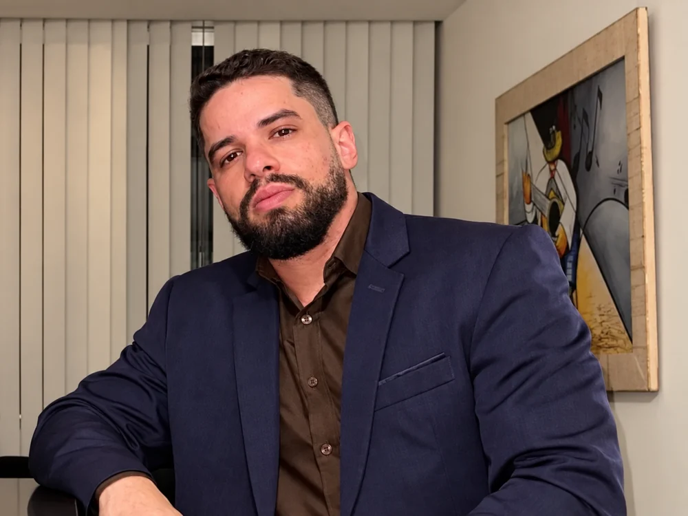 Retrato de Matheus Kehl no escritório, com persianas e quadro ao fundo